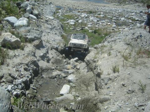 1987 Suzuki Samurai - A white 1987 Suzuki Samurai tackles a challenging off-road course through a rocky, dry stream bed.