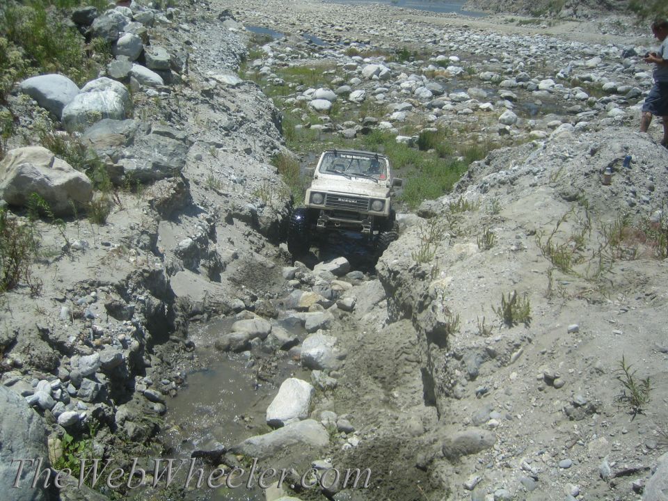 White 1987 Suzuki Samurai navigating a rocky stream bed