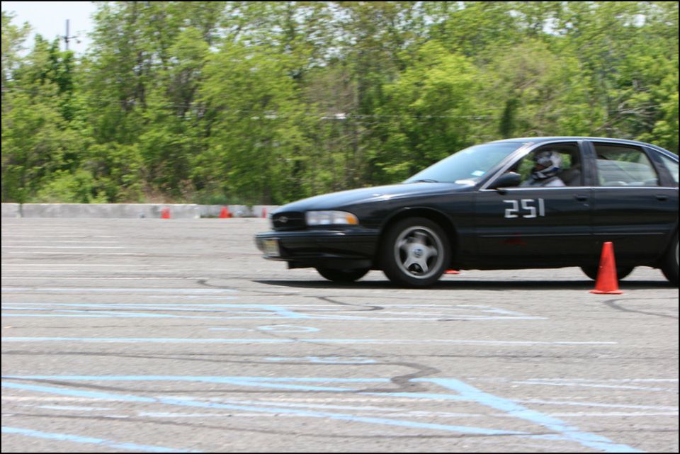 Black sedan, number 251 on door, driving on a paved lot with orange cones