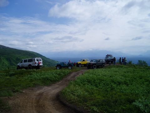 2000 Ford E350 - A group of off-road vehicles are gathered on a scenic hilltop overlooking a vast landscape under a cloudy sky.
