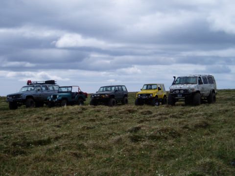 2000 Ford E350 - A group of off-road vehicles are parked on a grassy hill with a cloudy sky above.