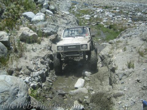 1987 Suzuki Samurai - A white 1987 Suzuki Samurai navigates a challenging off-road course with rocky terrain and water obstacles.