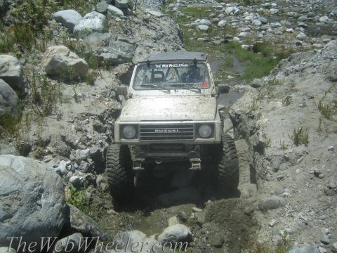 1987 Suzuki Samurai - This Suzuki Samurai is shown navigating a challenging off-road course with mud and rocks.