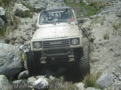 1987 Suzuki Samurai - Suzuki Samurai tackling a challenging off-road path with mud and rocks.