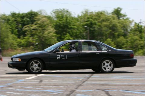 2001 Mercury Grand Marquis - A black sedan with racing numbers is captured in motion on a track during an event.