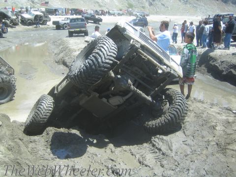 1987 Suzuki Samurai - An off-road vehicle is stuck in a mud pit, with several people observing the scene.