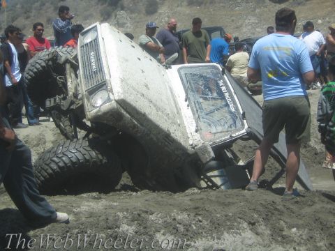 1987 Suzuki Samurai - A Suzuki Samurai is stuck in the mud, tilted on its side, with onlookers gathered around.