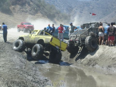 1987 Suzuki Samurai - Off-road vehicles tackle a muddy obstacle course with spectators watching.