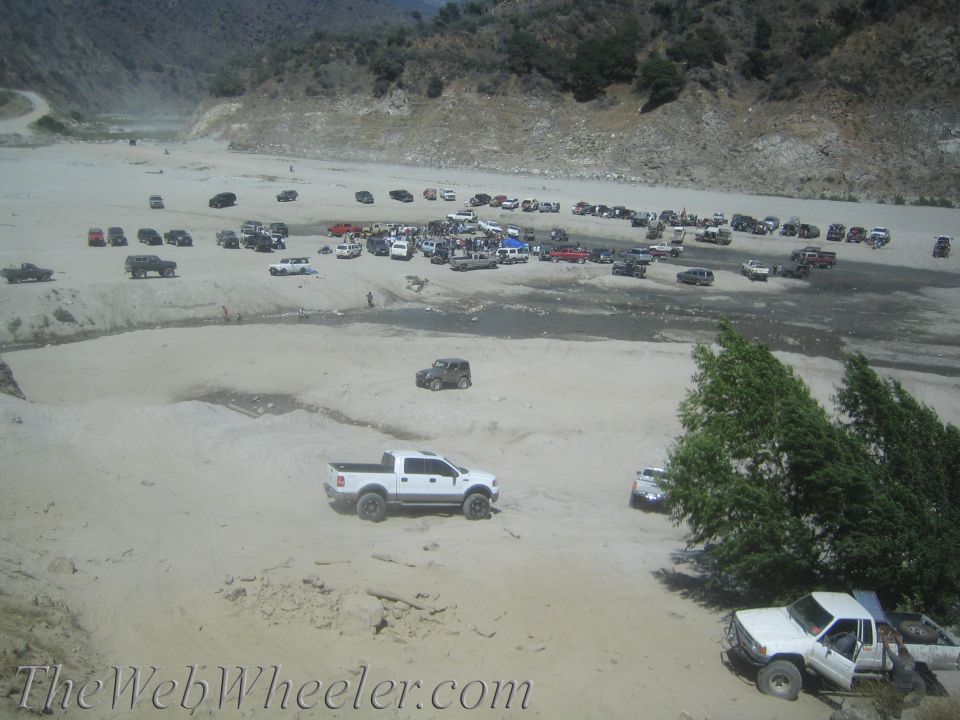 many trucks and SUVs parked and driving in a sandy, mountainous area
