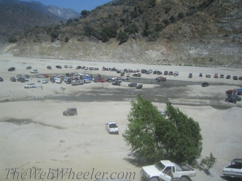 1987 Suzuki Samurai - A group of off-road vehicles are gathered in a dry riverbed, with mountains in the background.