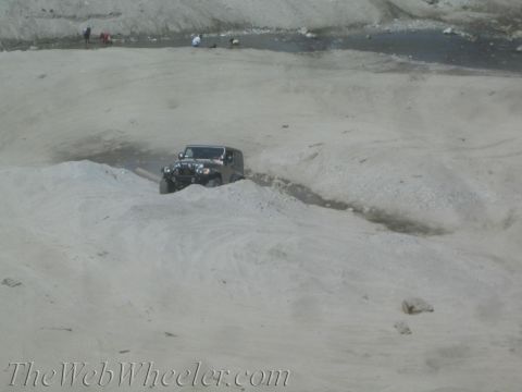 1987 Suzuki Samurai - A dark-colored Jeep Wrangler navigates a sandy terrain, kicking up dust as it drives through a wash.