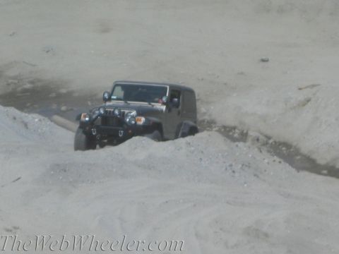 1987 Suzuki Samurai - Jeep Wrangler driving through a dirt path with mounds of sand on either side.