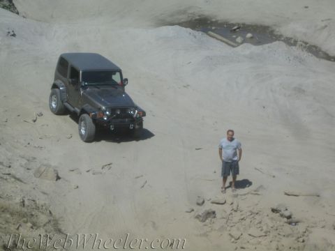 1987 Suzuki Samurai - A man stands beside a Jeep Wrangler in a dusty, off-road environment.
