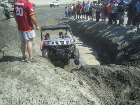 1987 Suzuki Samurai - A UTV attempts to drive through a challenging muddy trench with onlookers observing the action.