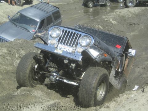 1987 Suzuki Samurai - A modified Jeep CJ-7 navigates a muddy off-road course, with another vehicle partially submerged in the background.