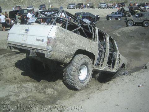 1987 Suzuki Samurai - A heavily modified off-road vehicle navigates a sandy, muddy terrain with spectators in the background.