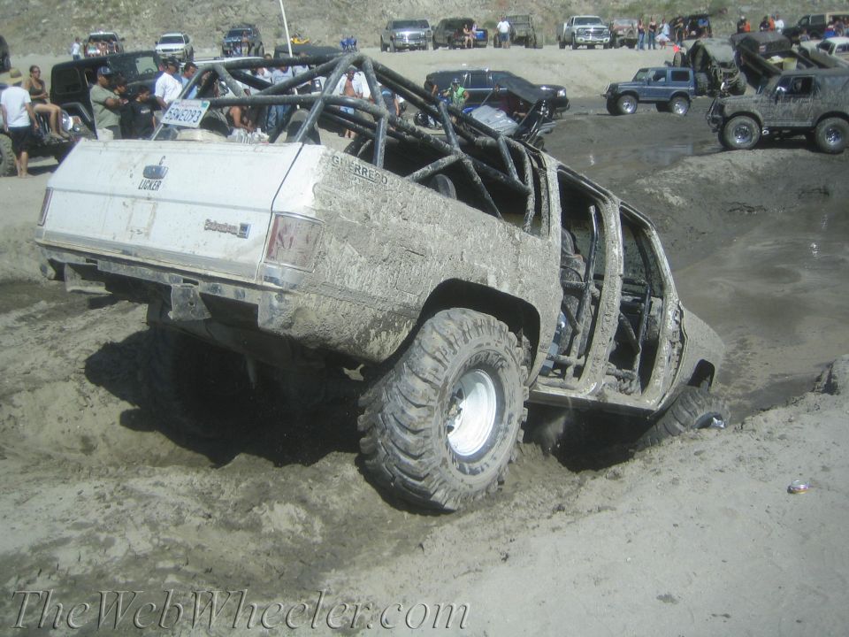 Mud-covered off-road vehicle with roll cage, missing doors, stuck in sand