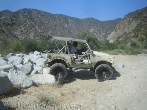 1987 Suzuki Samurai - A driver navigates a , rocky terrain in a modified off-road vehicle under a clear blue sky.