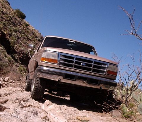 1996 Ford Bronco - A tan Ford F-Series truck navigates a challenging, rocky terrain under a clear blue sky.