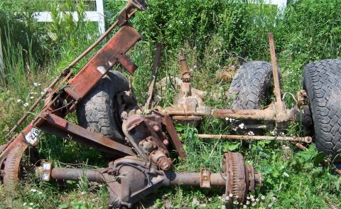 1980 Jeep CJ5 - Discarded vehicle axles and tires are seen in a grassy area, suggesting a junkyard setting.