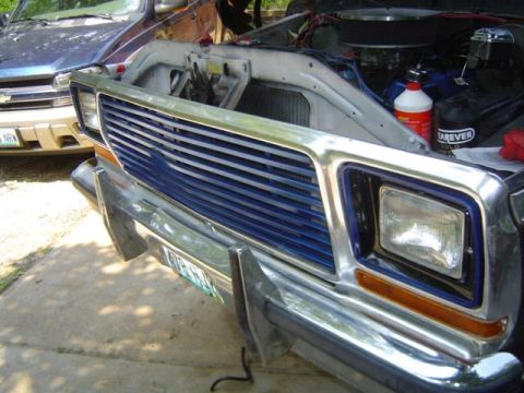 1979 Ford Bronco - The front of a 1978 Ford Bronco is visible, with its hood open to reveal the engine bay and a blue Chevrolet parked behind it.