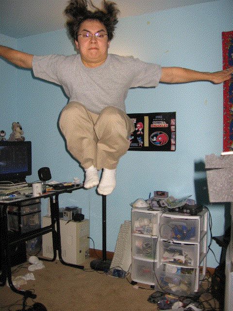 1991 Ford Bronco - A person is captured mid-jump in a cluttered room, with a computer setup and various storage units visible.