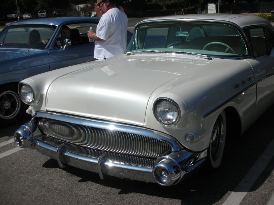 White 1955 Buick Special two-door hardtop, front view, chrome grille, fender skirts, parked next to a blue car