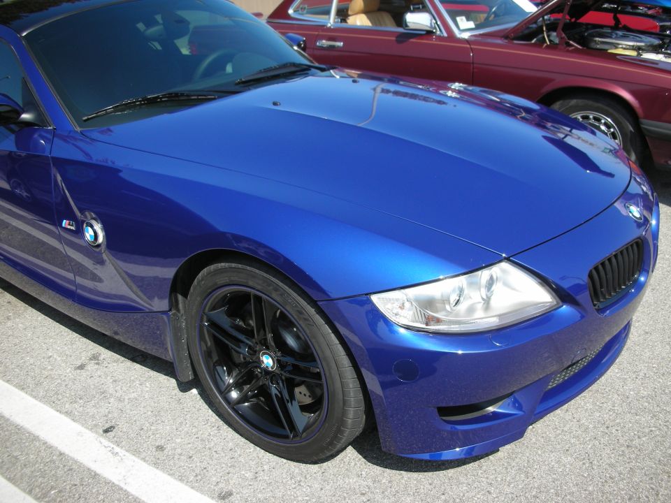 Blue BMW Z4 front quarter view with black wheels and a maroon car in the background