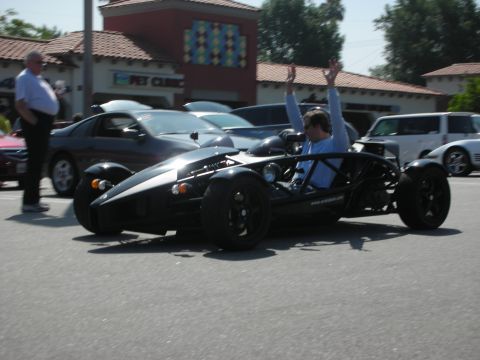 1998 Ford Crown Victoria - A driver in a black Ariel Atom with arms raised celebrates at a car meet.