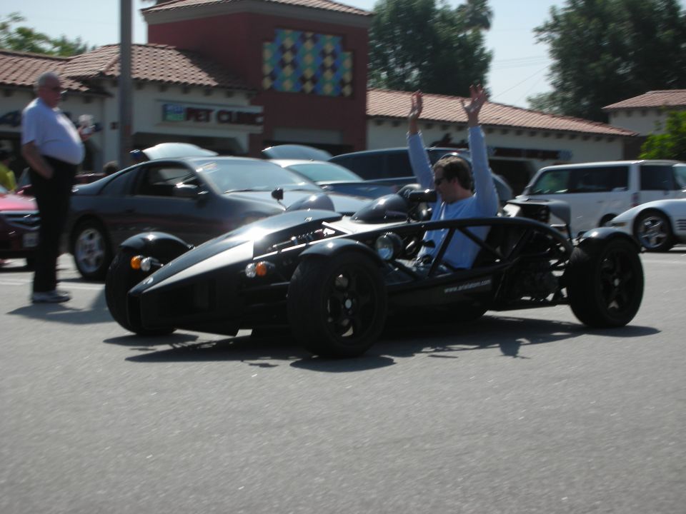 Black Ariel Atom with driver raising arms, seen from front-right