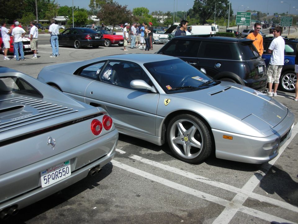 Two silver Ferraris parked in a lot, one in foreground, other in background. People milling around