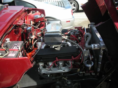 1998 Ford Crown Victoria - The engine bay of a red car is open, revealing a V8 engine and other components. A silver car is parked behind it.