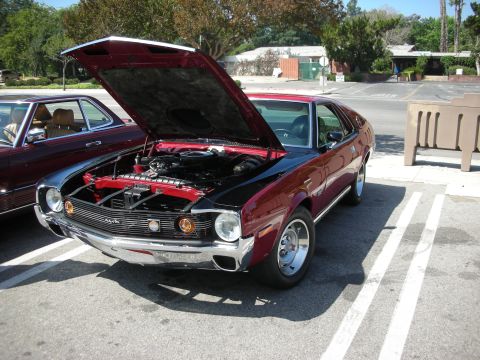 1998 Ford Crown Victoria - A maroon and black 1970 AMC AMX is parked with its hood open, next to another maroon car.