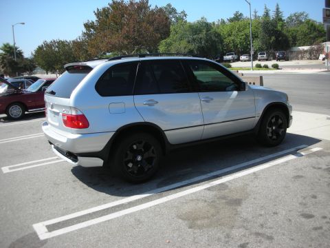 1998 Ford Crown Victoria - A silver BMW X5 is parked in a lot next to another vehicle.