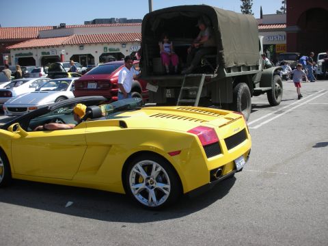 1998 Ford Crown Victoria - A yellow convertible sports car is parked in a lot with other vehicles and people.