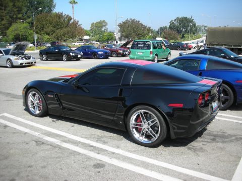 1998 Ford Crown Victoria - A black Chevrolet Corvette C6 with pink racing stripes is parked in a lot next to other vehicles.