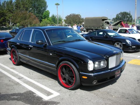 1998 Ford Crown Victoria - Black sedan with custom red wheels parked at a car meet, other vehicles present.