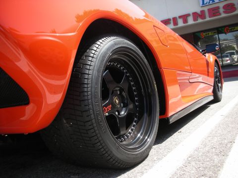 1998 Ford Crown Victoria - An orange sports car is parked outside a fitness center, its custom black wheels with red 'Corse' lettering.