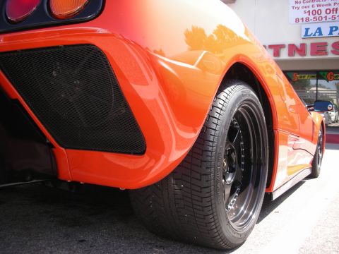 1998 Ford Crown Victoria - Close-up of an orange sports car's rear wheel and fender, parked outdoors.