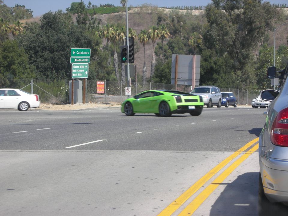 Green sports car turning at intersection, other cars and traffic signs visible