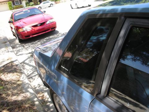 1998 Ford Crown Victoria - A red Ford Mustang is parked on a residential street, with another vehicle visible in the foreground.