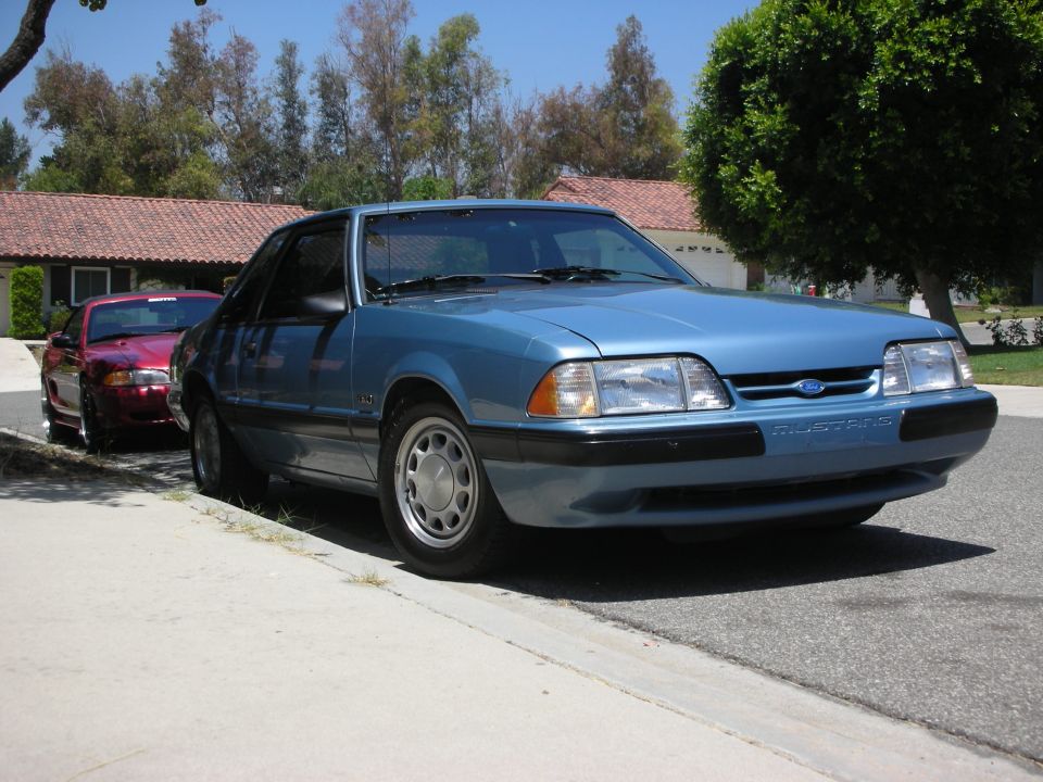 Blue Ford Mustang parked on street, red car behind it