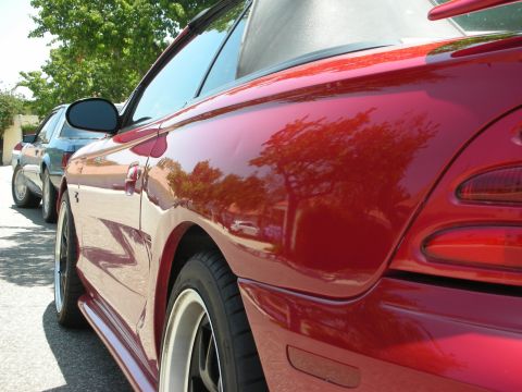 1998 Ford Crown Victoria - A red convertible sports car is parked next to another vehicle on a sunny day.