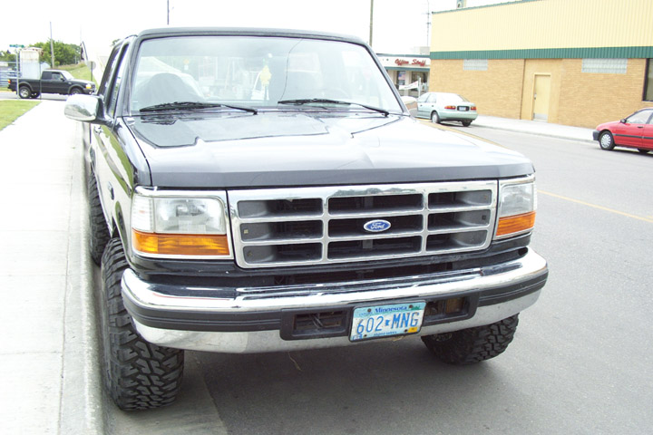 Dark lifted Ford Bronco front view with bar grille, hood deflector and mud tires