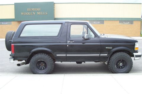 1996 Ford Bronco - Side view of a black 1996 Ford Bronco parked in front of a building.