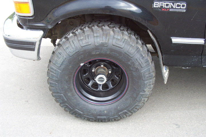 Black Ford Bronco front wheel with mud-terrain tire and black steel rim on pavement