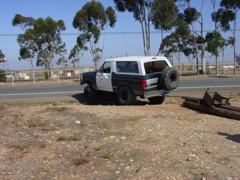 Ford Bronco parked on dirt road, two-tone black and white paint, spare tire mounted on rear door