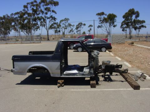1994 Ford Bronco - This stripped-down truck body sits on wooden blocks in a parking lot under a clear blue sky.