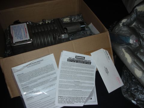 1998 Ford Crown Victoria - A supercharger and associated installation manuals are shown inside a cardboard box, with a Kenne Bell label on an envelope.