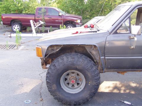 1989 Ford F-250 - A gray truck with a large off-road tire is parked next to a maroon Dodge Ram pickup.